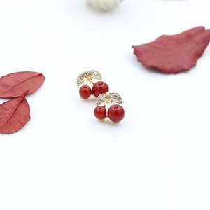 Macro shot of cute gold-plated cherry earrings with crystal leaf accents and red beads