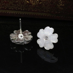 Close-up of white five-petal flower earrings with glitter finish and crystal center