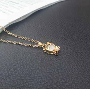 Nahaufnahme des goldenen Katzenanhängers mit weißem Opal auf schwarzem Leder