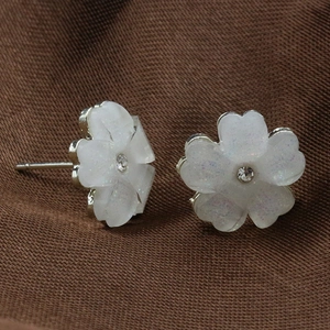 Macro view of white five-petal flower stud earrings with shimmering glitter and center crystal