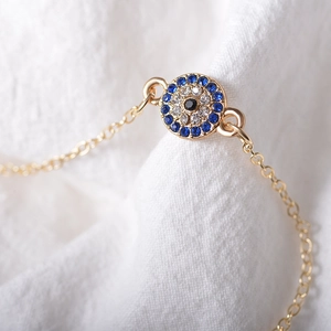 Makro-Detail des goldenen Evil Eye Fußkettchens mit blauen und weißen Zirkonia-Steinen