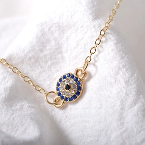 Elegantes goldenes Fußkettchen mit blauem bösem Blick und Zirkonia auf Stoff