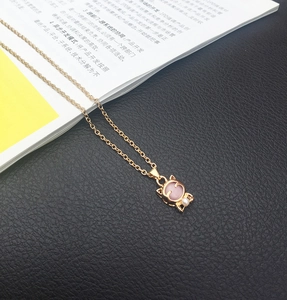 Detailaufnahme von goldener Katzen-Halskette mit rosa Edelstein und kleiner Perle