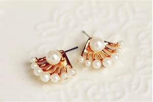 Détail des boucles d'oreilles dorées en éventail avec perles blanches sur fond texturé