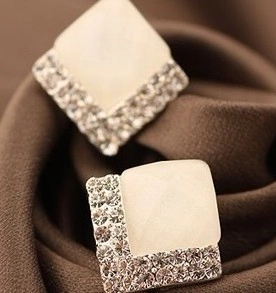 Macro shot of square cream cat eye earrings with pavé rhinestones on brown silk fabric