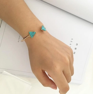 Detail of a gold-finish open bangle featuring marble-textured triangle stones on wrist