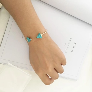 Detailed view of golden C-shaped cuff bracelet with triangular turquoise stones on wrist