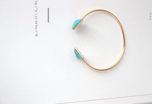 Macro detail of gold-toned open bangle with blue triangle turquoise stones and marble texture