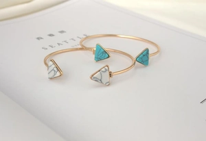 Detail of gold open bangles with marble and turquoise triangle stones on a magazine