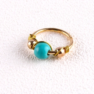 Handmade gold nose ring with turquoise bead and wire wrapping on white background