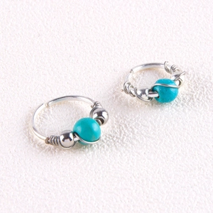 Macro view of silver wire-wrapped piercing jewelry featuring turquoise stone beads