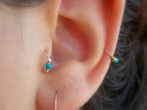 Macro detail of three turquoise beaded wire hoop earrings worn on conch and tragus