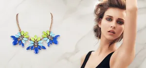 Detailansicht einer goldenen Statement-Halskette mit blau-grünen Kristallen an einem Model