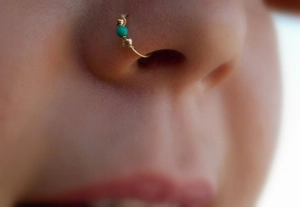 Close-up of wire-wrapped turquoise nose ring with two gold beads on a model