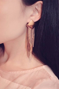 Detail view of long rose gold tassel earrings with geometric studs on a female model
