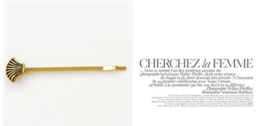 Detailed view of a golden shell-shaped hair clip on an editorial fashion magazine background