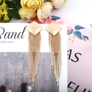 Detail of long gold geometric fringe earrings with metal chains and bars on white board