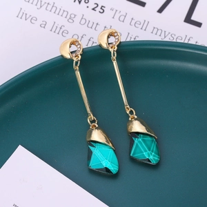 Close-up of elegant gold long drop earrings with green crystal on dark ceramic plate