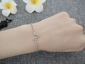 Minimalist silver heartbeat pulse bracelet worn on wrist with floral background