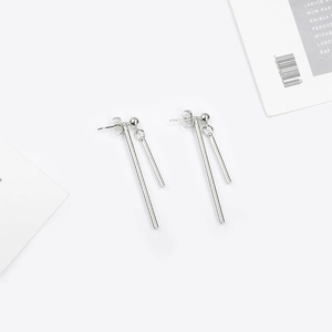 Détail de boucles d'oreilles barres asymétriques argentées avec sphères polies sur fond blanc