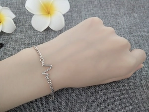 Detail shot of a silver heartbeat pulse charm bracelet worn on a woman's wrist