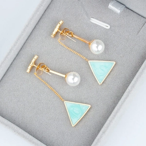 Detail of golden geometric drop earrings with white pearl and light blue triangle charm