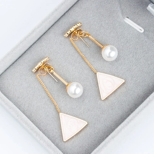 Close-up of gold tassel earrings with pink enamel triangles and round white pearls