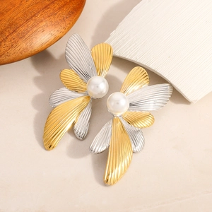 Two-tone gold and silver flower wing earrings with large pearls on beige surface