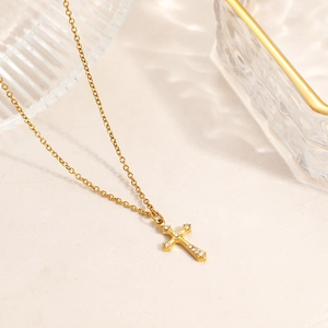 Detail of gold cross necklace featuring sparkling zircon stones on stone background