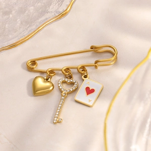 Gold safety pin brooch with heart, key, and Ace of Hearts pendants on marble surface