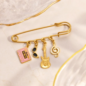 Golden music theme brooch with pink cassette, guitar and note charms on a marble base