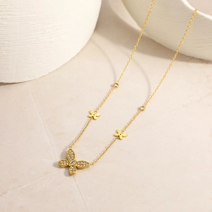 Dettaglio di collana a farfalla in oro 18K con pietre su superficie di pietra