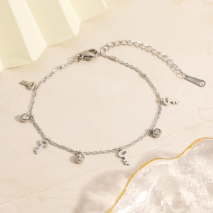 Elegant stainless steel bracelet with key charms and round zircon crystals on marble surface