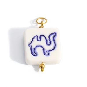 Close-up of square white ceramic pendant featuring blue camel silhouette with gold bail