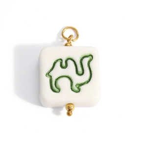 Detail of white square pendant featuring a green camel motif and gold-tone metal beads