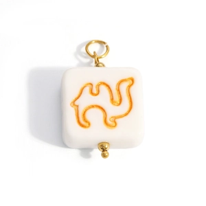 Close-up of square cream pendant with golden camel motif and metallic hanging loop