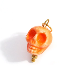 Macro detail of skull pendant in orange resin with golden metallic loop and bead accents