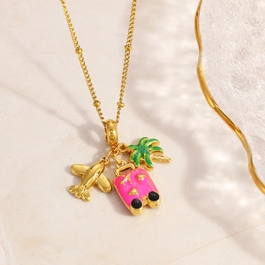 Close-up of golden necklace featuring enamel airplane, suitcase, and palm tree charms