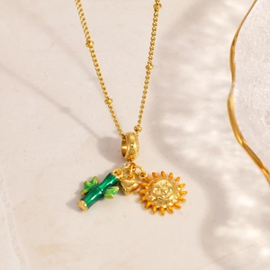 Detail of gold beaded necklace featuring cactus, heart and sun charms on marble