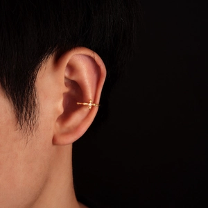 Stylish gold cross ear cuff with a small zircon stone worn on a model against black background