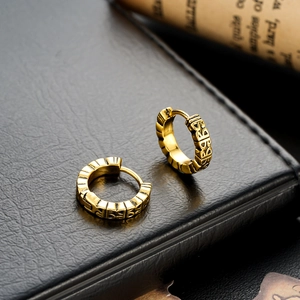 Vintage gold hoop earrings with embossed texture on black leather and scroll background