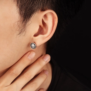 Close-up of a silver lion head relief stud earring worn on a male ear model