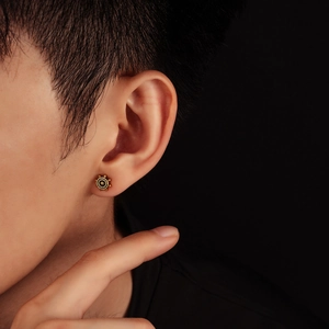 Retro golden ship wheel stud earring worn by male model on a black background