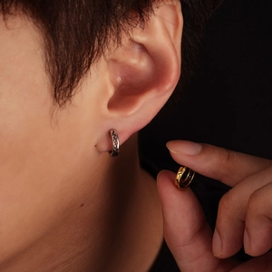 Minimalist silver and gold heart patterned earrings shown on ear and held by hand