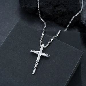Silver cross pendant necklace with geometric textures and box chain on black rock