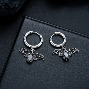 Detailed close-up of Gothic bat earrings with black gemstone on leather background