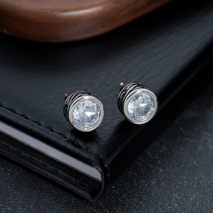 Macro shot of silver zircon stud earrings with intricate side scrollwork on black leather