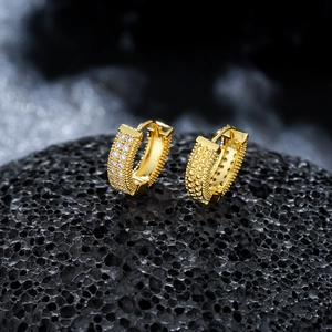 Détail de boucles d'oreilles créoles dorées serties de zircons et bordure perlée