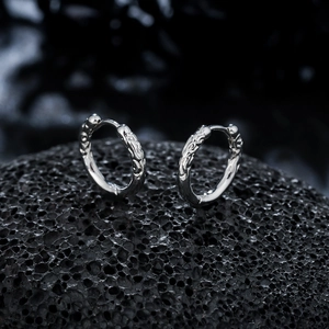 Macro detail of silver hoop earrings featuring intricate dragon pattern on dark volcanic rock