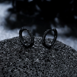 Detail of black hoop earrings with embossed texture on dark volcanic rock background